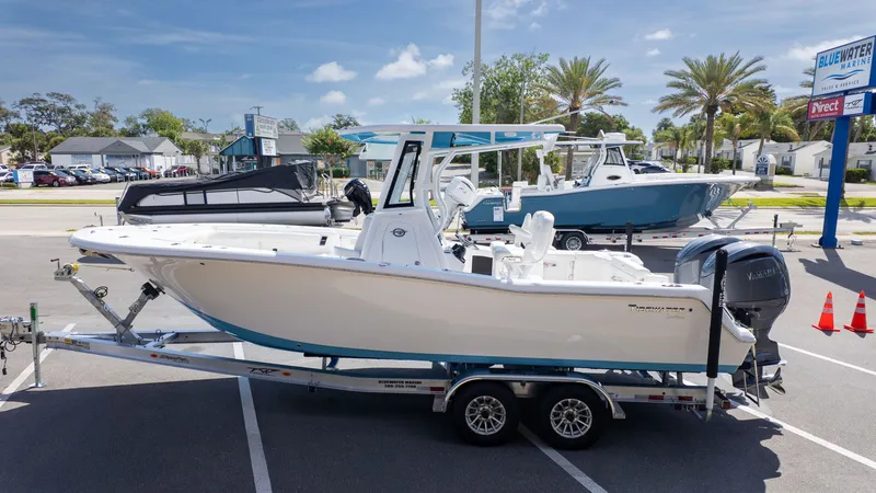 The Image of A Tidewater 256 CC Adventure boat on a trailer in a parking lot, surrounded by palm trees. - 1