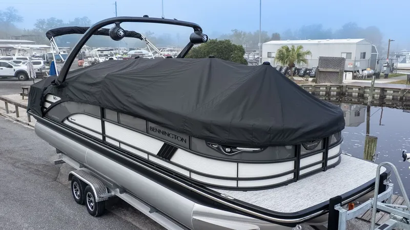 Slide: The Image of 2026 Bennington 26 M STERN LOUNGE on a trailer, covered in black, at a marina. - 24