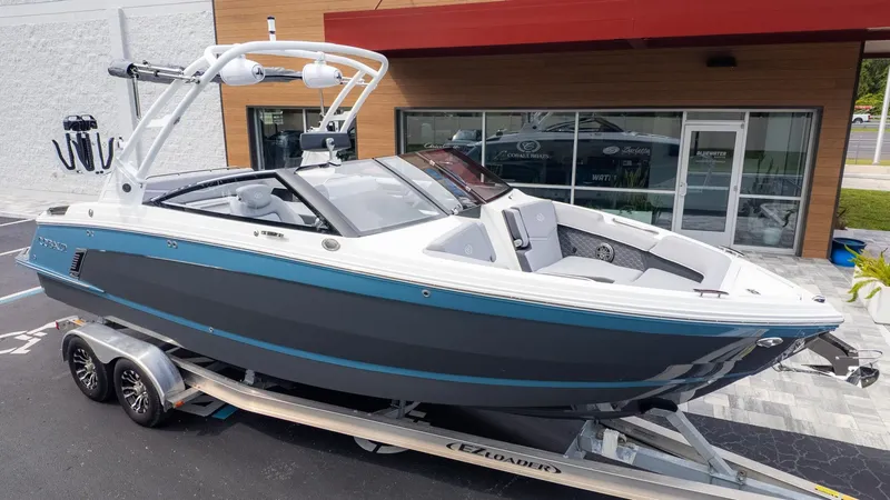 The Image of A 2026 Cobalt R6 Surf boat on a trailer in front of a modern building. - 1