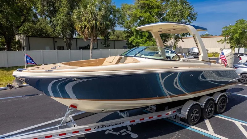 The Image of A sleek 2025 Chris-Craft Launch 28 GT boat on a trailer, surrounded by trees. - 1