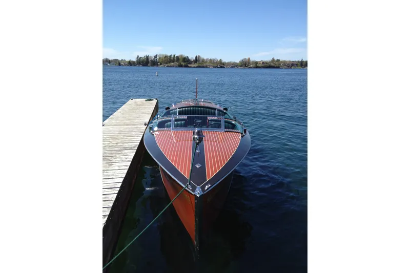 Slide: The Image of 1996 Hacker-Craft Triple Cockpit Runabout docked on a serene lake. - 6