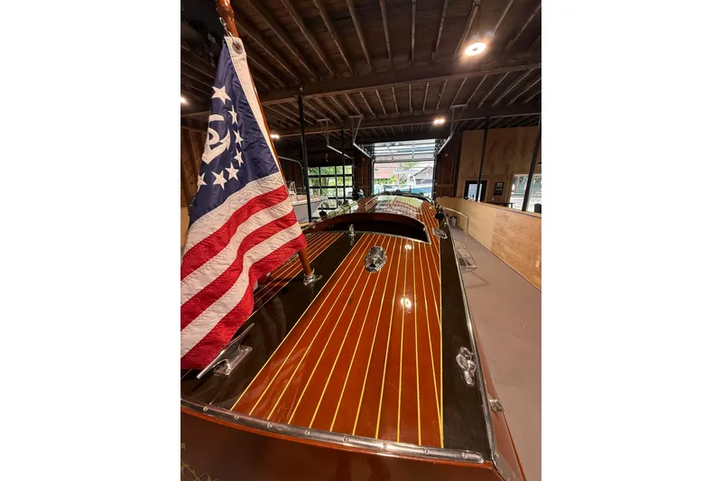 Slide: The Image of 1996 Hacker-Craft Triple Cockpit Runabout with American flag, showcased indoors. - 3