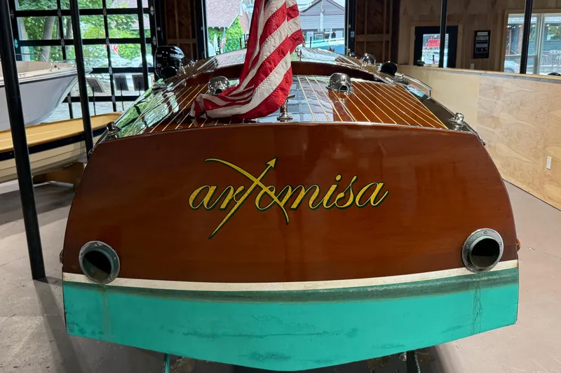Slide: The Image of 1996 Hacker-Craft Triple Cockpit Runabout with American flag, named "Artemisa," in a showroom. - 16