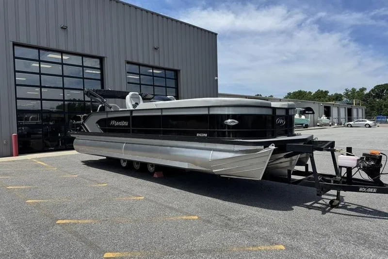 Slide: The Image of 2026 Manitou Encore 25 SL SHP pontoon boat parked outside a large garage. - 8