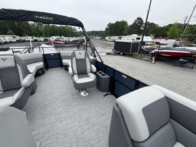 Slide: The Image of Viaggio Lago V22U pontoon boat with gray upholstery and bimini top, parked in a lot. - 26