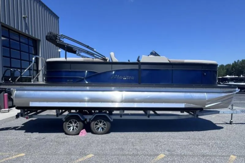 The Image of 2027 Manitou Aurora 23 RF SHP pontoon boat on trailer, parked outdoors. - 1