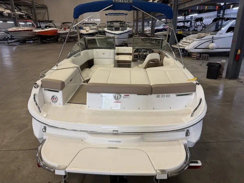 Slide: The Image of A 2015 Cobalt 200 boat in a storage facility. It features a blue sunshade and white upholstery. - 9