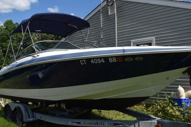 Slide: The Image of 2006 Cobalt 240 boat on trailer, parked beside a house under a blue sky. - 1