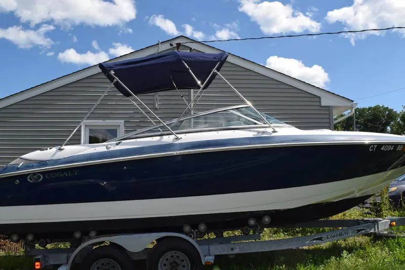 The Image of 2006 Cobalt 240 boat on trailer, parked near a house under a blue sky. - 0