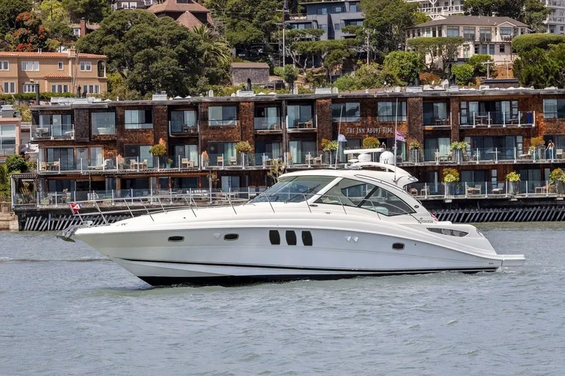 Slide: The Image of A white 2007 Sea Ray 48 Sundancer cruising on the water near a modern waterfront. - 1