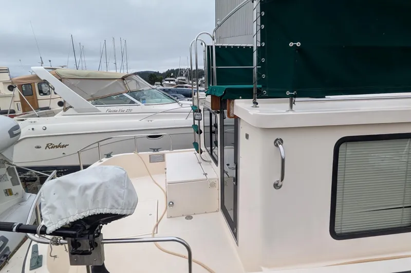 Slide: The Image of 1998 Nordic Tug 32 docked, featuring green canopy and adjacent boats in marina. - 3
