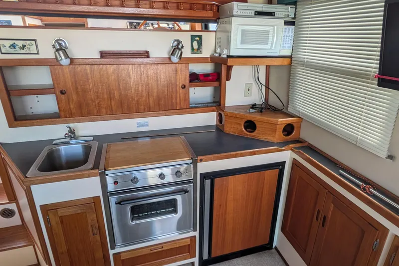 Slide: The Image of Compact kitchen in a 1998 Nordic Tug 32, featuring wood cabinetry, sink, stove, and microwave. - 20