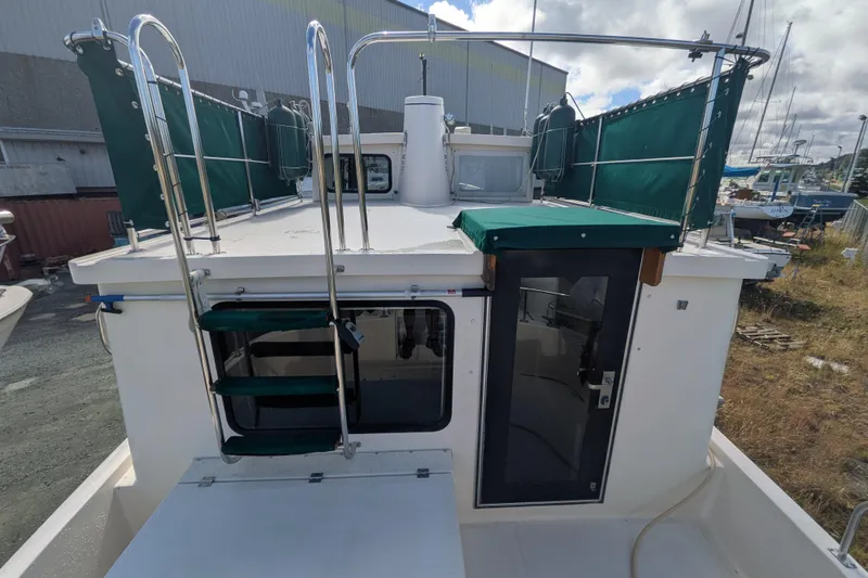 Slide: The Image of 1998 Nordic Tug 32 boat with green canvas, docked outdoors under cloudy skies. - 6