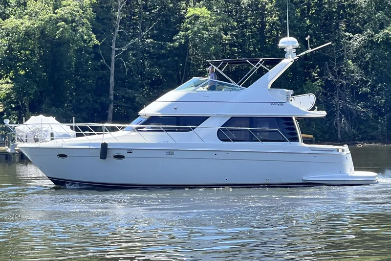 Slide: The Image of 2003 Carver 450 Voyager Pilothouse yacht cruising on a serene lake with lush forest backdrop. - 3