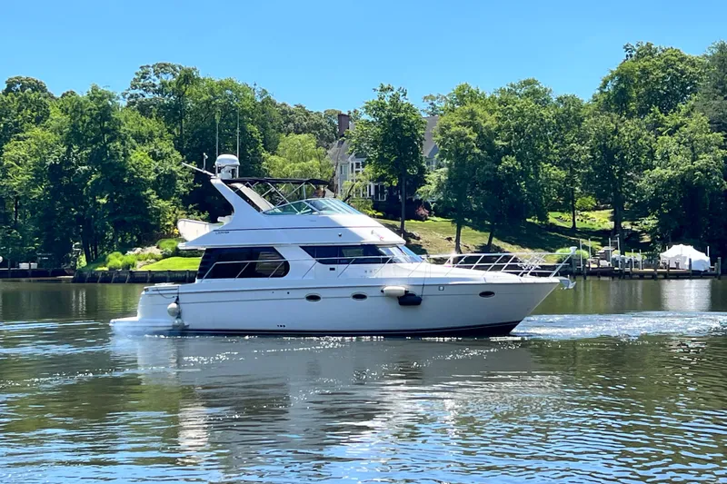 The Image of 2003 Carver 450 Voyager Pilothouse yacht cruising on a serene lake with lush greenery. - 0
