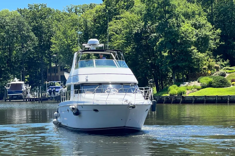 Slide: The Image of 2003 Carver 450 Voyager Pilothouse yacht cruising on a serene lake with lush greenery. - 2
