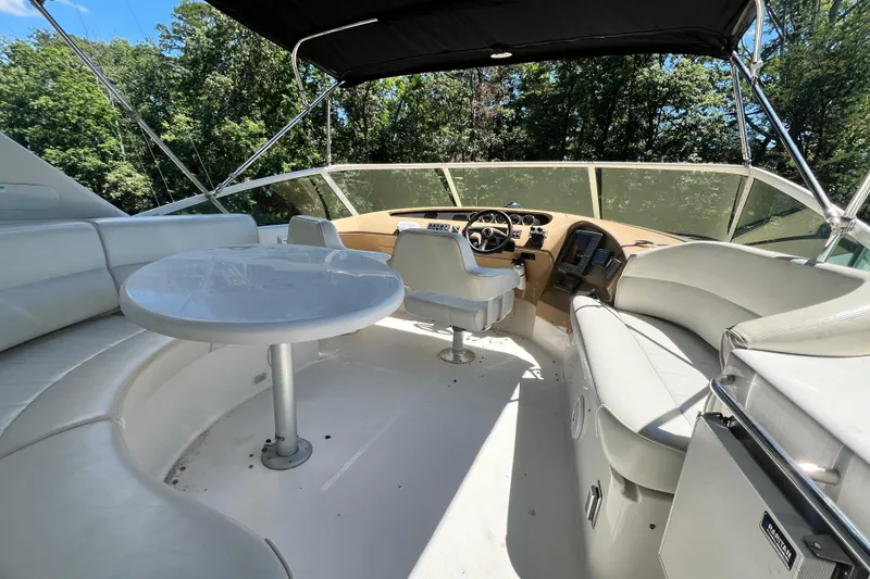 Slide: The Image of 2003 Carver 450 Voyager Pilothouse interior with seating and helm, surrounded by lush greenery. - 43