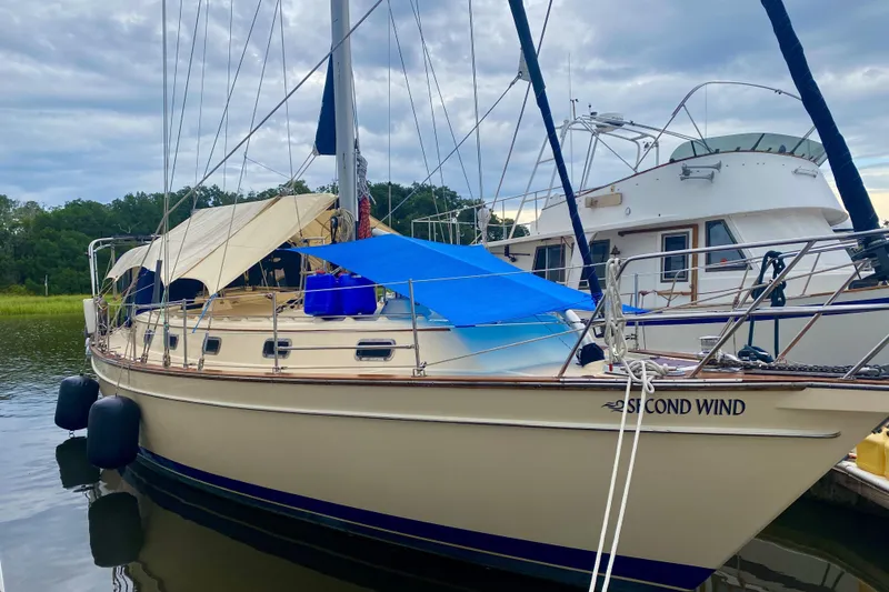 Slide: The Image of 2006 Island Packet 440 sailboat docked, featuring beige hull and blue canopy under cloudy skies. - 11