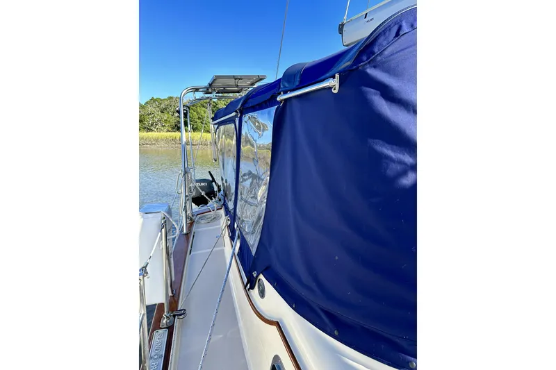 Slide: The Image of 2006 Island Packet 440 sailboat with blue canopy, docked by a serene waterway. - 22