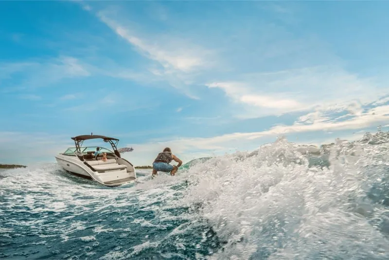 Slide: The Image of A Sea Ray SLX 260 Surf boat navigates choppy waters as a person surfs nearby. - 12