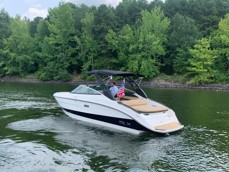 Slide: The Image of A sleek 2026 Sea Ray SLX 260 Surf boat cruising on a calm lake, surrounded by lush trees. - 15