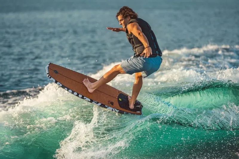 Slide: The Image of A man surfs on a wave behind a boat. He is wearing a life vest and shorts. - 11