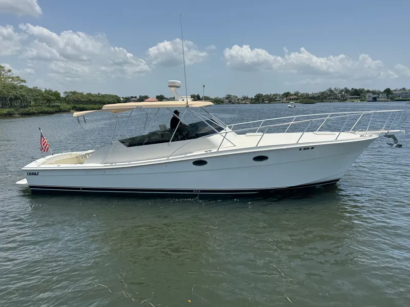 The Image of A 1990 Topaz Royale boat on calm water with a shaded canopy and a US flag. - 0