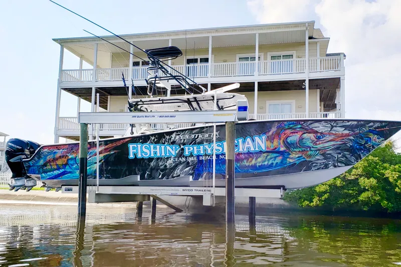 Slide: The Image of Freeman 42LR 2020 boat with vibrant fish-themed wrap, docked near a waterfront house. - 3