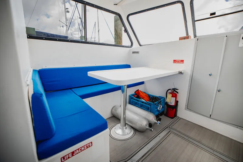 Slide: The Image of Interior of a dive boat with blue seating, table, fire extinguisher, and life jackets. - 15
