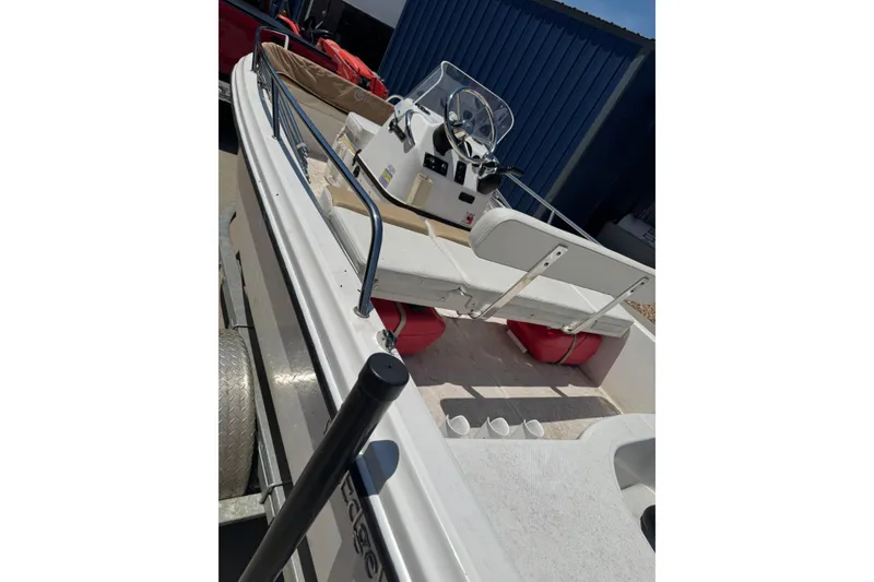 Slide: The Image of 2018 Edgewater 158CS boat with white interior and steering console, docked near a blue building. - 2