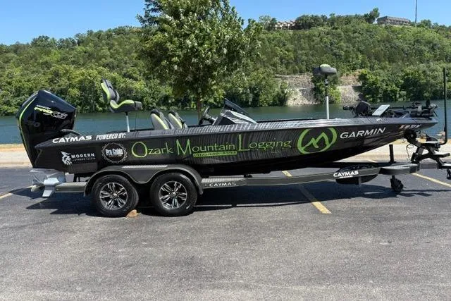 The Image of 2023 Caymas CX 20 PRO boat with Ozark Mountain Logging branding, parked by a scenic river. - 0
