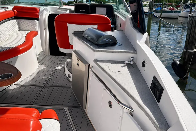 Slide: The Image of 2012 Rinker 310 Express Cruiser LE interior with red and white seating, kitchenette, and water view. - 12