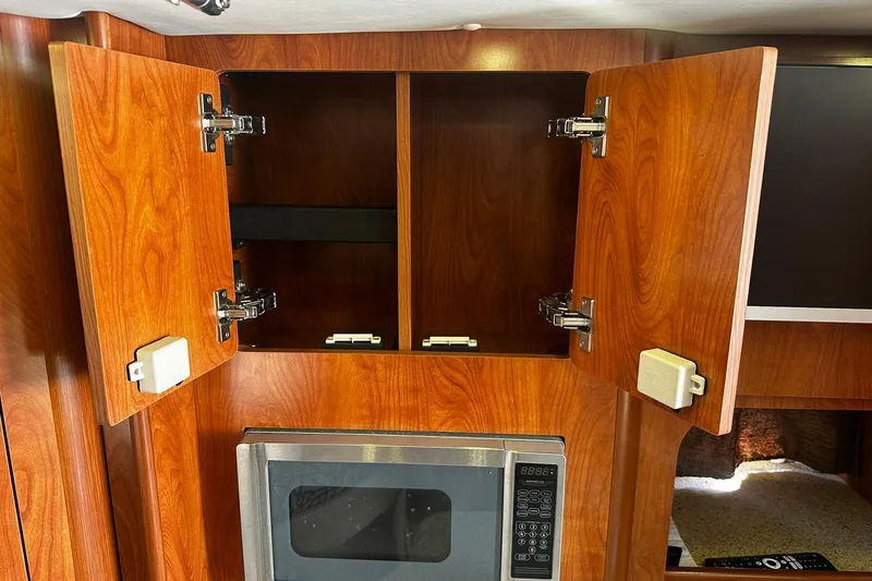 Slide: The Image of Interior of 2012 Rinker 310 Express Cruiser LE with open wooden cabinets and microwave. - 49