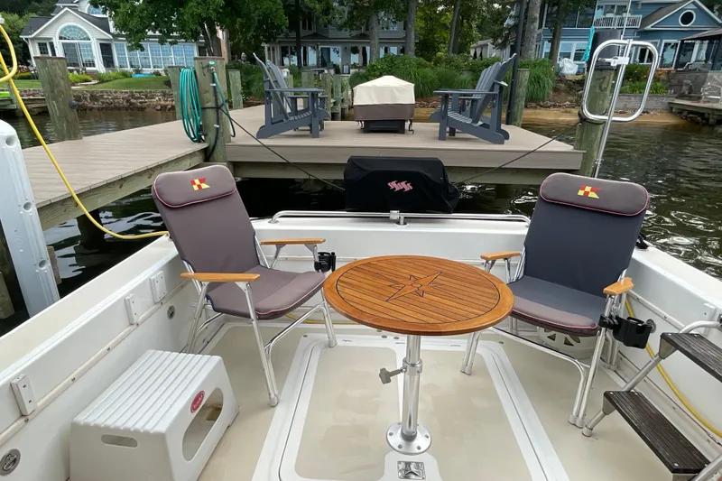 Slide: The Image of Fox Island Thirty Sedan Cruiser 2005 with chairs and table, docked by a lakeside deck. - 5