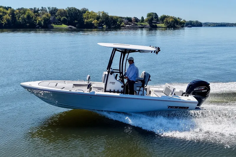 Slide: The Image of 2027 Pathfinder 2200 Hybrid boat cruising on a serene lake with lush green shoreline. - 27