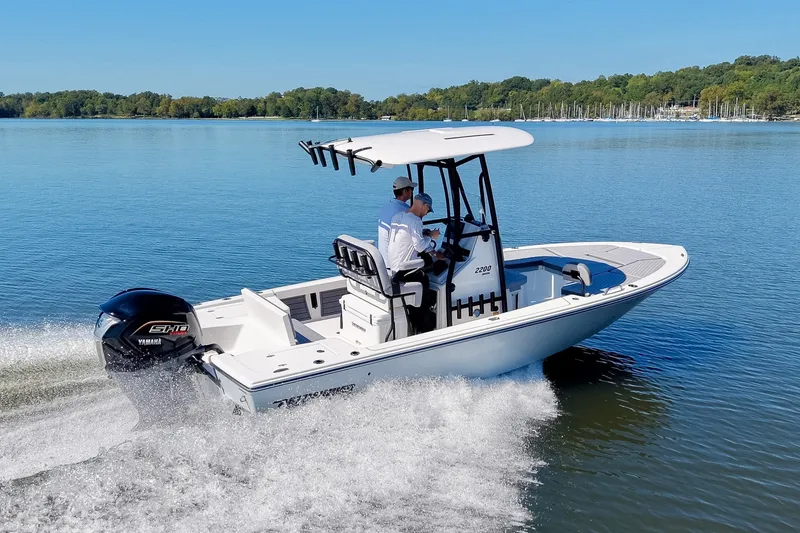 Slide: The Image of 2027 Pathfinder 2200 Hybrid boat cruising on a serene lake with lush green shoreline. - 29