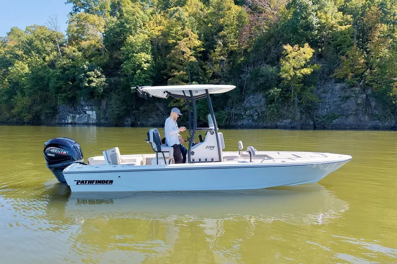 Slide: The Image of 2027 Pathfinder 2200 Hybrid boat on a calm lake with lush green trees. - 24