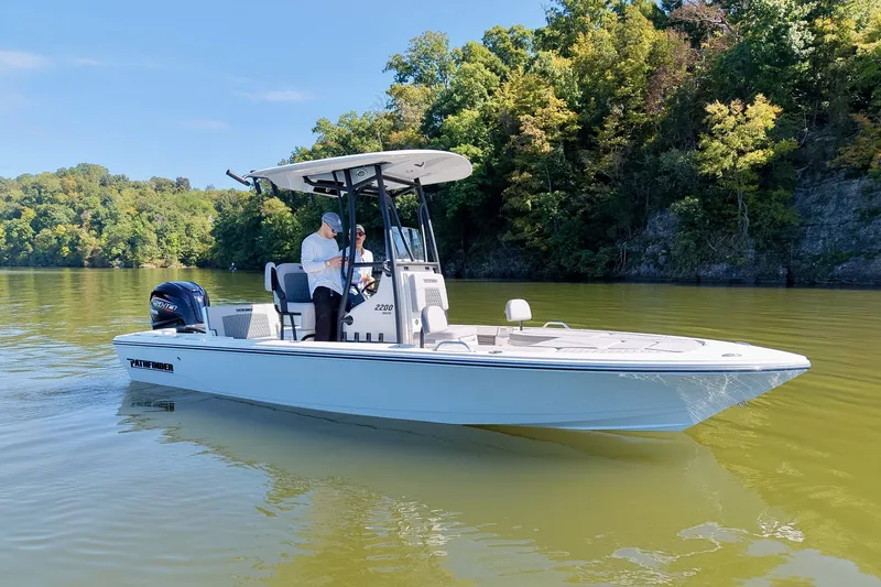 Slide: The Image of 2027 Pathfinder 2200 Hybrid boat cruising on a scenic lake with lush green trees. - 2
