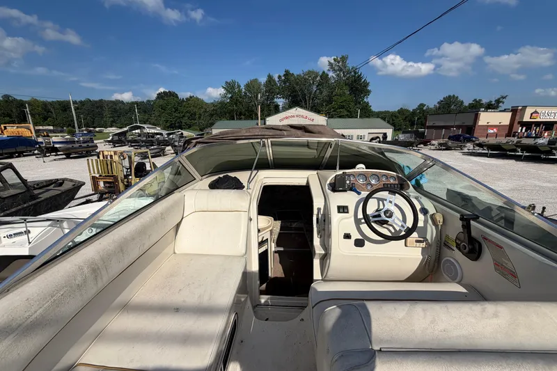 Slide: The Image of 1999 Sea Ray 240 Sundancer boat interior with steering wheel and seating, parked outdoors. - 11