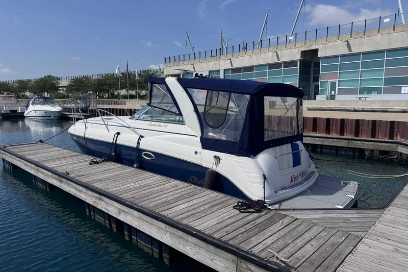 Slide: The Image of 2003 Rinker Fiesta Vee 312 boat docked at a marina with modern building backdrop. - 4