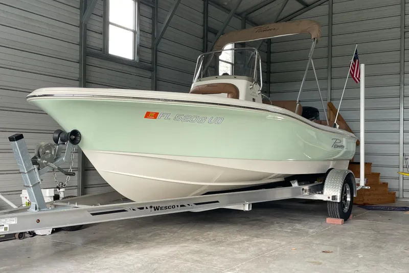 The Image of 2024 Pioneer 180 Islander boat on trailer in a garage, featuring sleek design and mint green hull. - 0