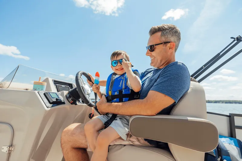 Slide: The Image of A man and child sit on a boat, both wearing sunglasses and smiling. - 13
