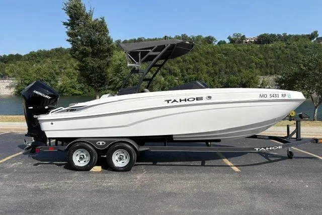 The Image of 2024 Tahoe T21 boat on trailer, parked near a scenic lake with lush greenery. - 0