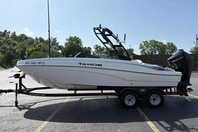 Slide: The Image of 2024 Tahoe T21 boat on trailer, parked outdoors, featuring sleek white design and Mercury outboard motor. - 2
