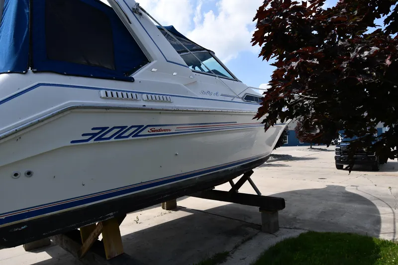 Slide: The Image of 1993 Sea Ray 300 Sundancer boat on dry dock, partially shaded by tree. - 6