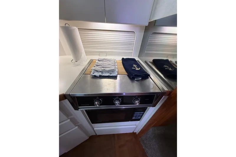 Slide: The Image of 1992 Carver 33 Aft Cabin Motor Yacht kitchen with stove and nautical-themed towels. - 37