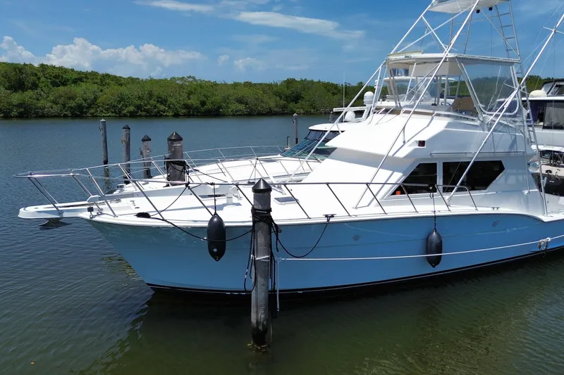 Slide: The Image of 1990 Hatteras 45 Convertible yacht docked on a calm river with lush greenery. - 17