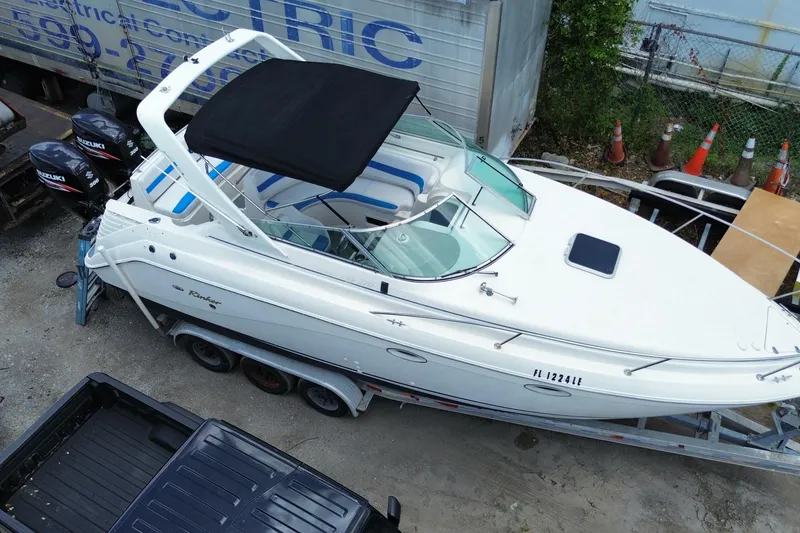 Slide: The Image of 2000 Rinker 280 Express Cruiser on trailer, white with blue accents, docked outdoors. - 5