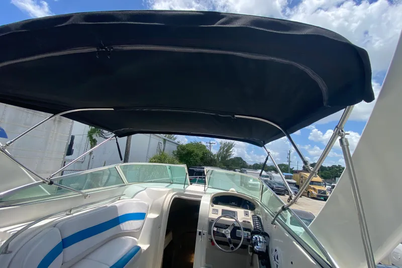 Slide: The Image of 2000 Rinker 280 Express Cruiser cockpit with canopy, steering wheel, and seating under blue sky. - 57