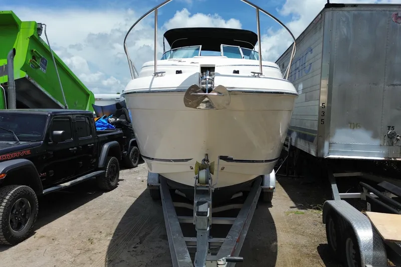 Slide: The Image of 2000 Rinker 280 Express Cruiser on trailer, parked between vehicles under a cloudy sky. - 19